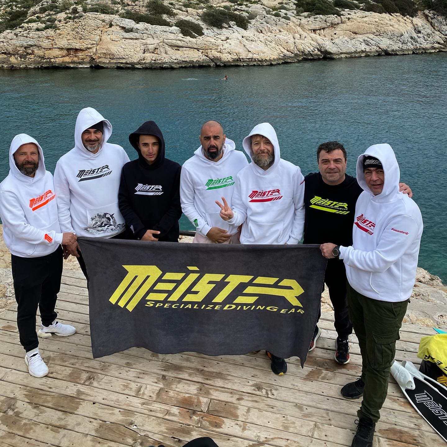 Meister community members holding a branded banner beside the sea